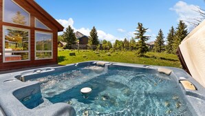 Een hottub met helder water, omgeven door een houten hut en een gazon met bomen.