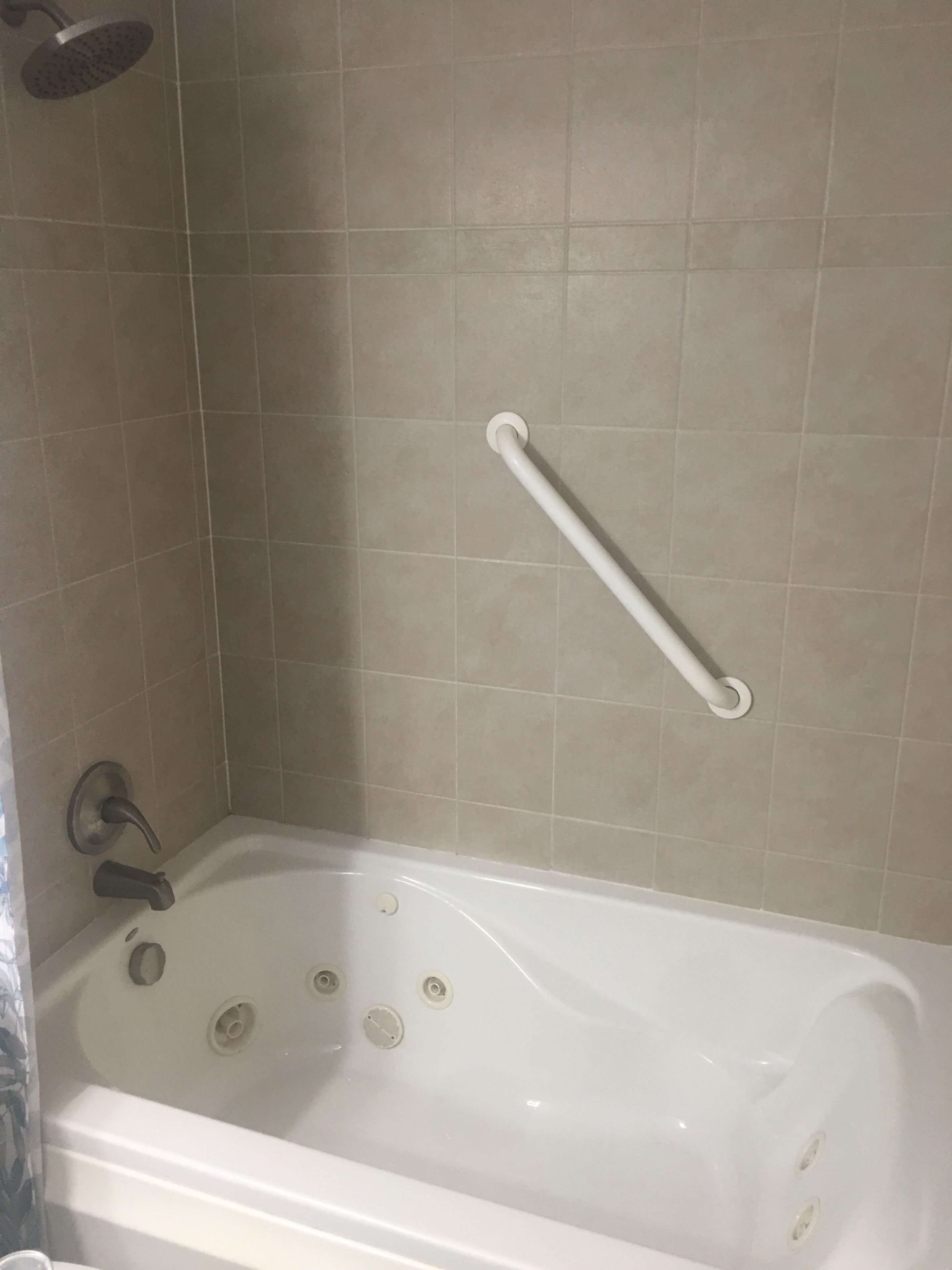 A bathtub with a grab bar, a showerhead, and a faucet.