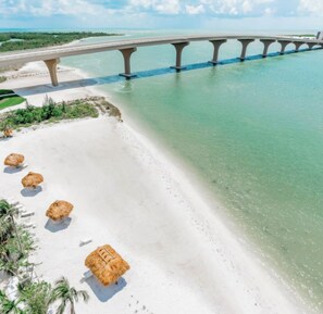 Ein Strand mit einer Brücke, klarem Wasser und Strandhütten aus Stroh.