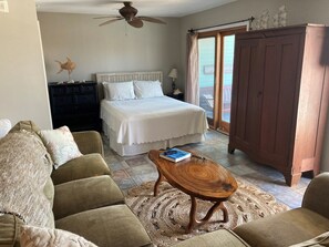 A bedroom with a bed, a wooden nightstand, a ceiling fan, a window with curtains, and a view of the outdoors. - Family Friendly & Quiet Riverside Condo with Pool & Fishing Piers (Pensacola)