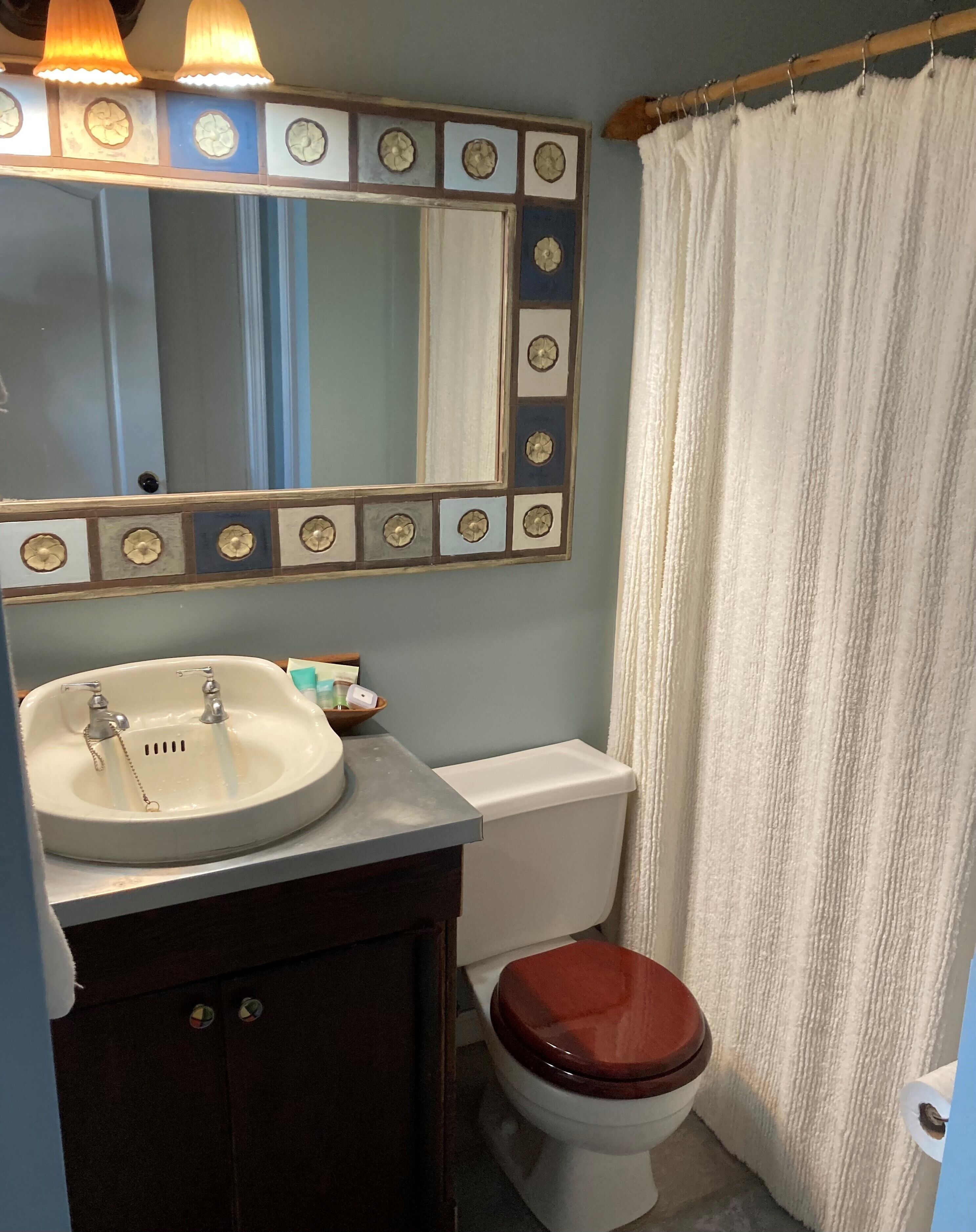 Un baño con lavamanos, espejo, inodoro y cortina de ducha.