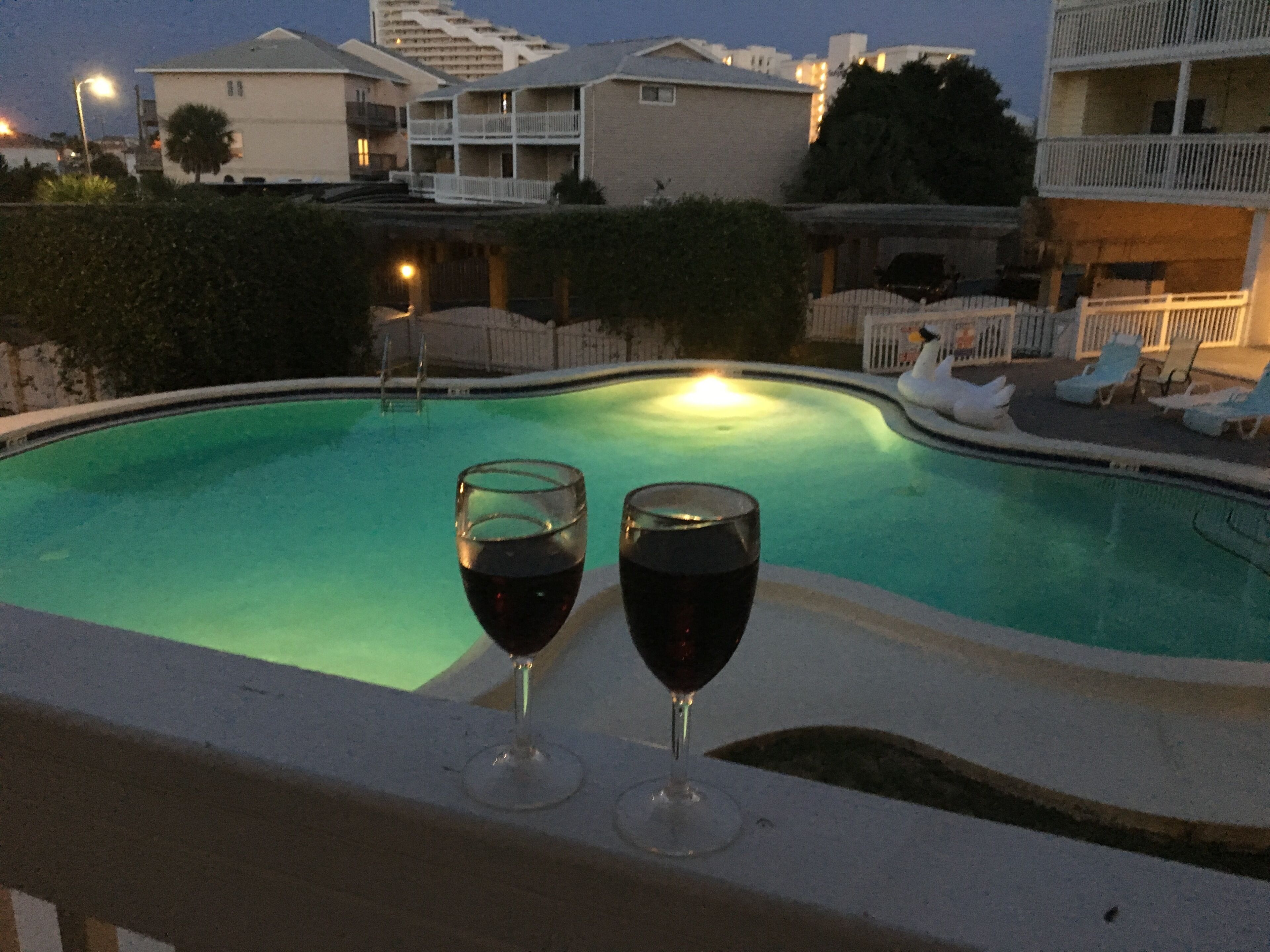 A swimming pool with two glasses of red wine on the edge.