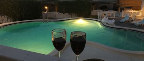 A swimming pool with two glasses of red wine on the edge.