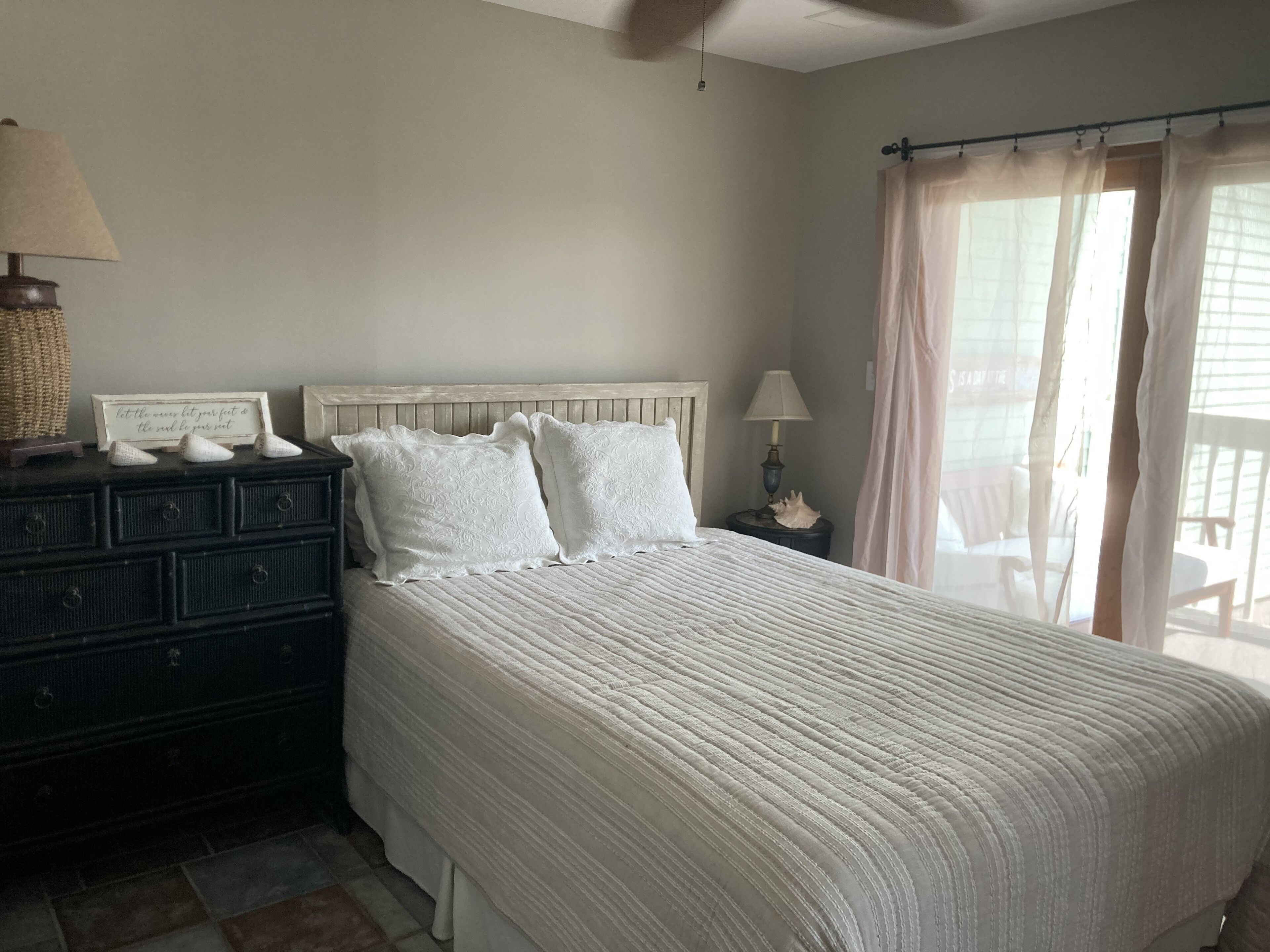 A bedroom with a bed, dresser, nightstand, lamp, and a window with curtains.