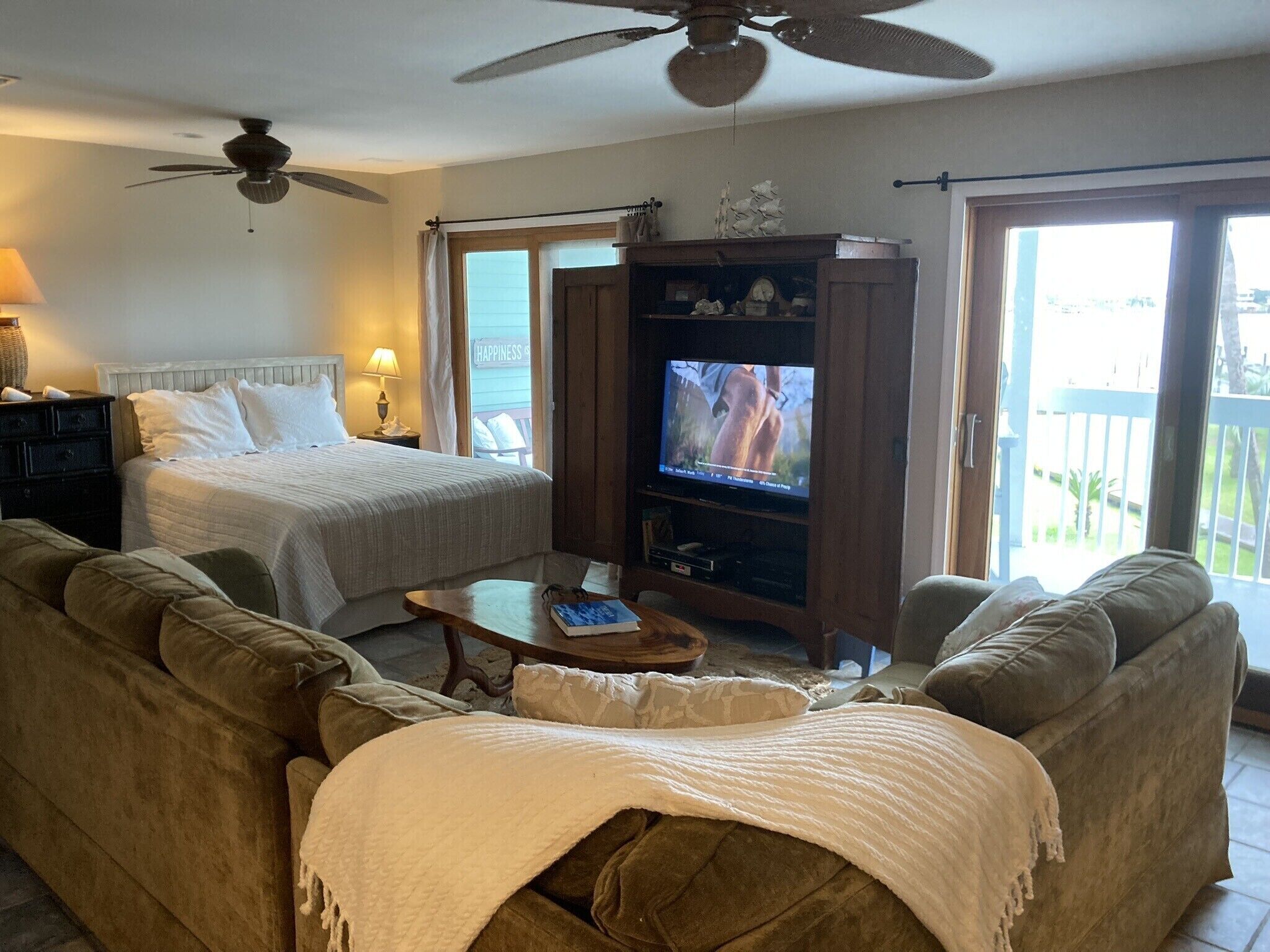 A room with a bed, a sofa, a television, and a ceiling fan.