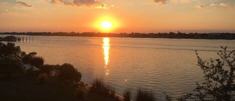 Un atardecer sobre una superficie de agua tranquila con una costa distante.
