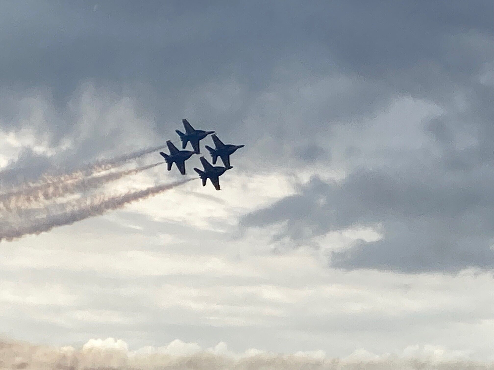Quatre avions de chasse volant en formation, laissant derrière eux des traînées de condensation sur un ciel nuageux.
