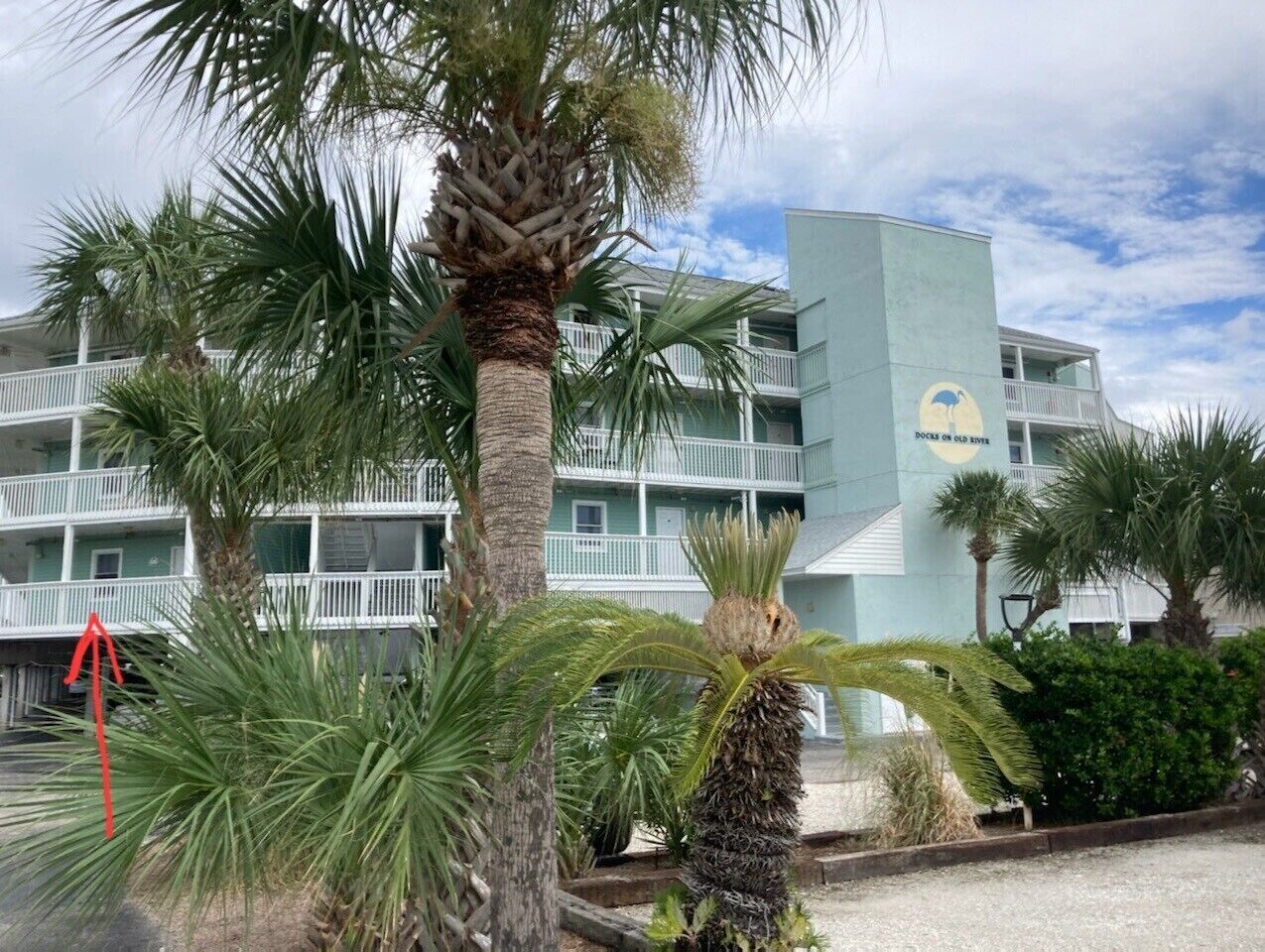 Un hotel con fachada azul claro, varios balcones y palmeras en primer plano.