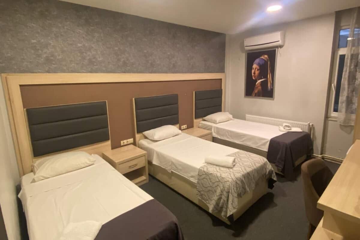 Quarto de hotel com três camas de solteiro, uma escrivaninha e uma cadeira.