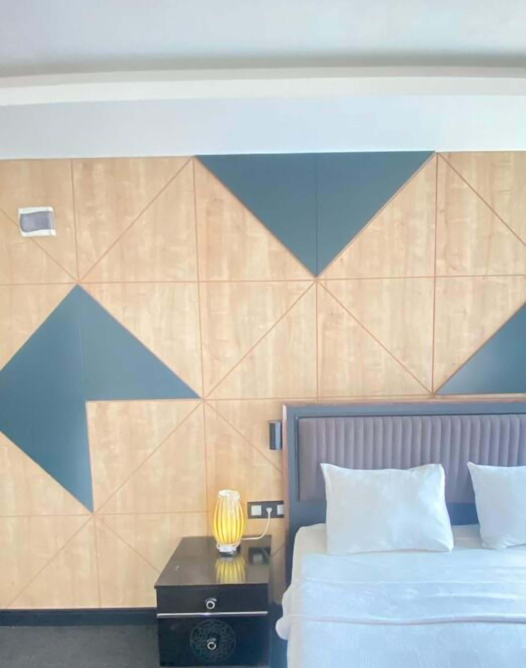 A hotel room with a bed, a nightstand with a lamp, and a geometric-patterned wall.