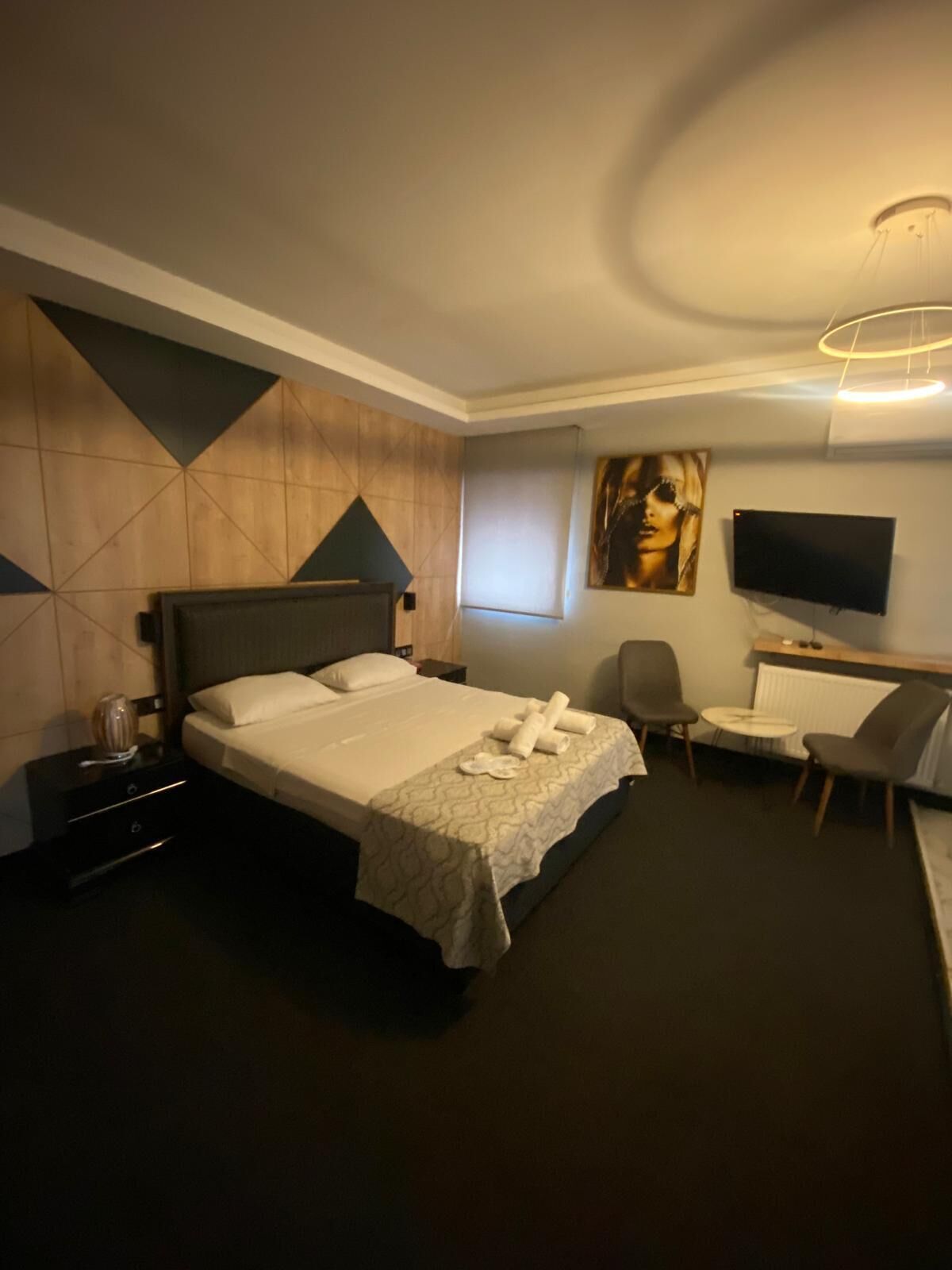 A hotel room with a bed, a desk, a chair, a TV, and a painting on the wall.