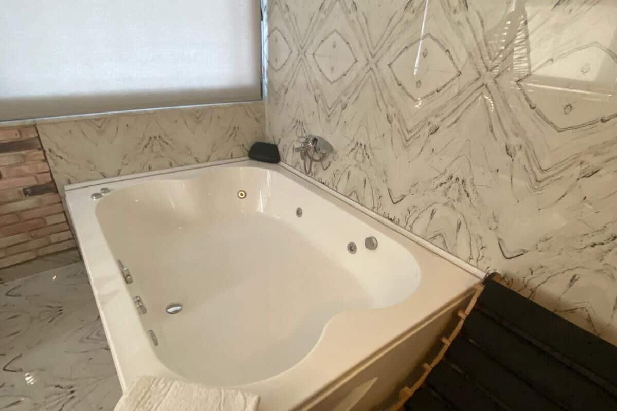 Uma banheira branca num quarto com paredes de mármore estampado e chão de madeira.