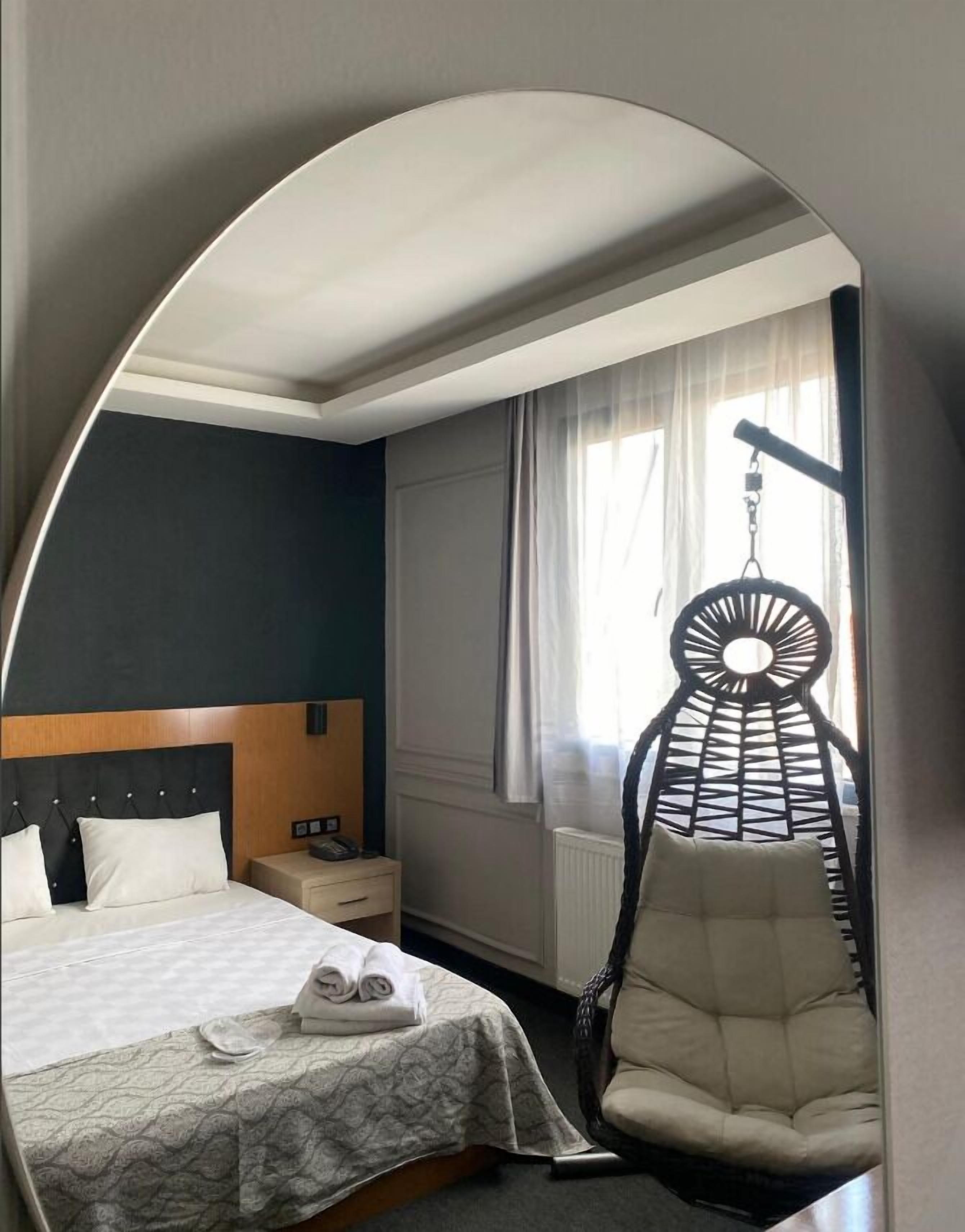 A hotel room with a bed, a hanging chair, a bedside table, and a window with curtains.