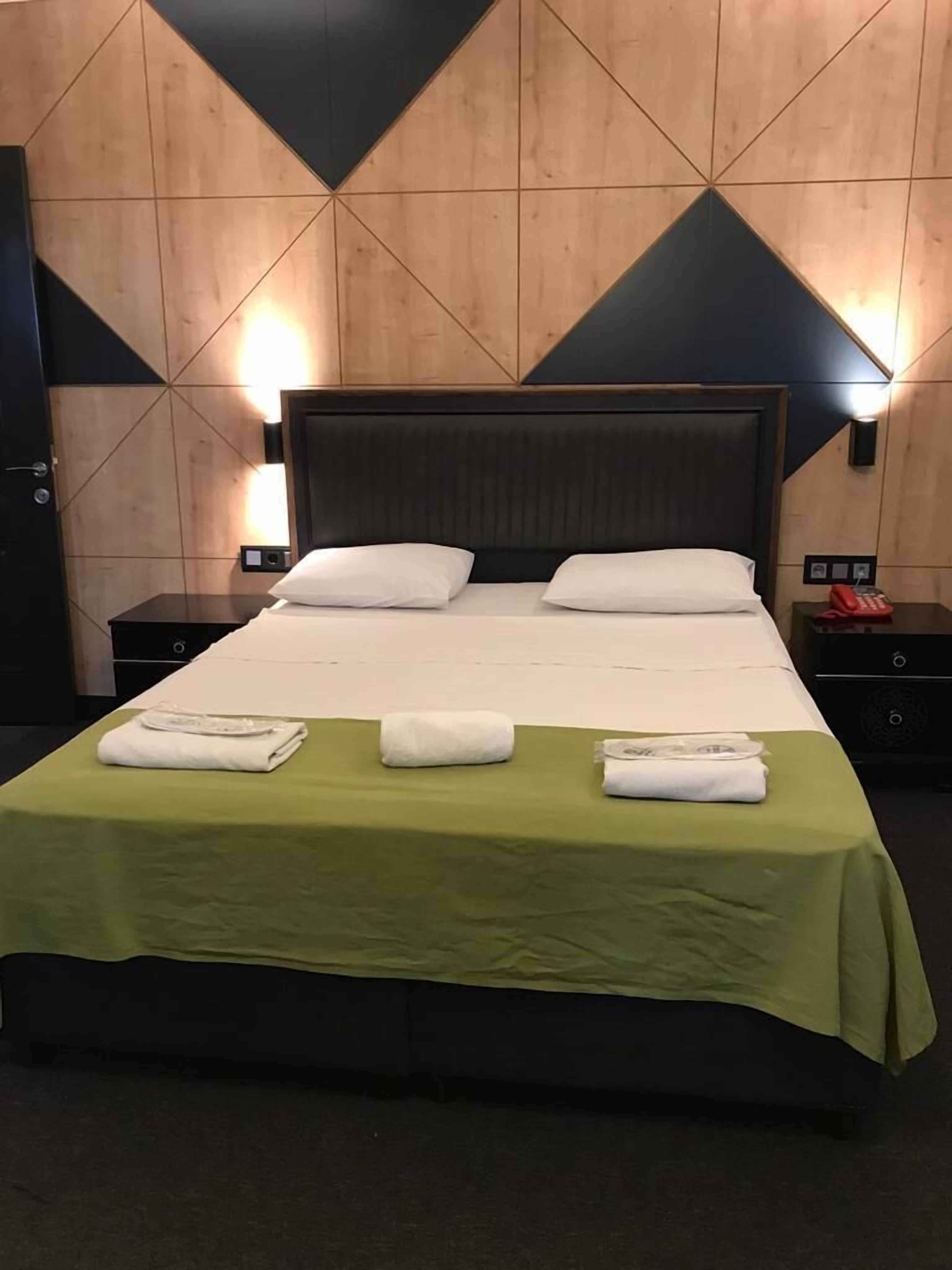 A hotel room with a large bed, green bedspread, two white pillows, and two nightstands with lamps.