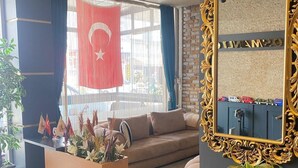 A hotel lobby with a sofa, a coffee table with flags, a mirror with a name plaque, and a large window with a flag. - Samsun Osmanli Otel (Samsun)