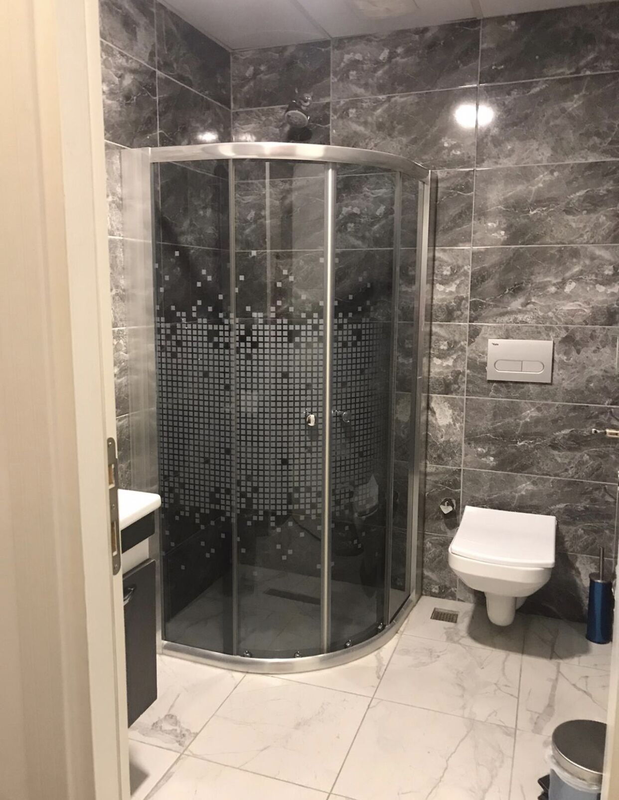 Une salle de bain moderne avec une douche à parois de verre, des toilettes blanches et un sol carrelé en marbre.