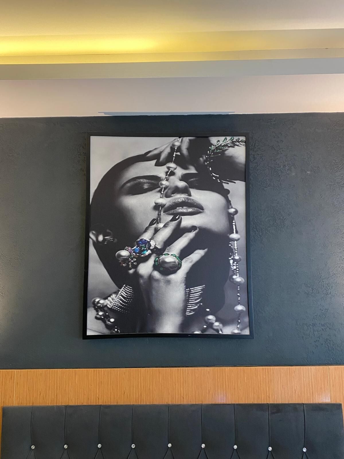 A framed black and white photograph of a person with elaborate jewelry on a wall.