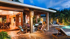 Una terraza de madera con sillones de descanso y zona de piscina, rodeada de vegetación tropical.
