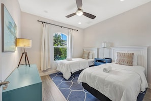 A hotel room with two beds, a ceiling fan, a window with curtains, a desk with a lamp, and a blue rug. - ISLAND LIFESTYLE FAMILY VACATION HOME SALT POOL (Naples)