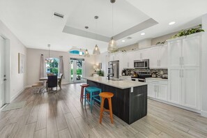 A modern kitchen with white cabinets, a central island, and bar stools.
