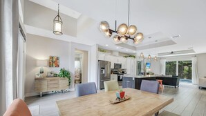 A spacious kitchen with modern appliances, a dining area with a wooden table, and a large island with seating. - ISLAND LIFESTYLE FAMILY VACATION HOME SALT POOL (Naples)
