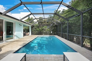 A swimming pool with a covered area, surrounded by trees and a building with glass doors. - ISLAND LIFESTYLE FAMILY VACATION HOME SALT POOL (Naples)