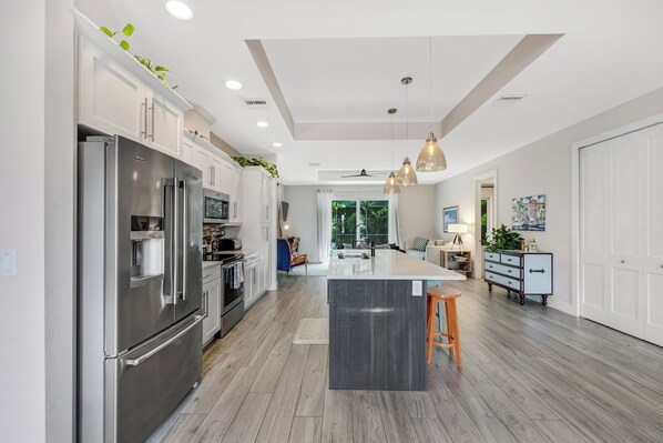 A modern kitchen with stainless steel appliances, a central island, and a dining area with a view of greenery. - ISLAND LIFESTYLE FAMILY VACATION HOME SALT POOL (Naples)