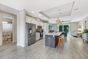 A modern kitchen with a central island, stainless steel appliances, and a dining area with a view. - ISLAND LIFESTYLE FAMILY VACATION HOME SALT POOL (Naples)