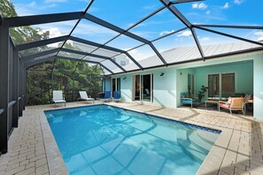 A swimming pool with a glass enclosure, surrounded by lounge chairs and a patio area.