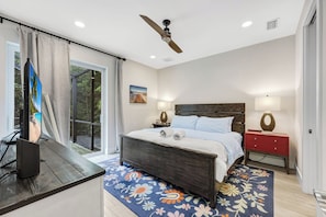 A bedroom with a bed, a nightstand, a desk with a computer, a ceiling fan, and a window with curtains.