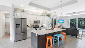 A modern kitchen with a central island, stainless steel appliances, and a large window offering a view of the outdoors. - ISLAND LIFESTYLE FAMILY VACATION HOME (BRAND NEW) (Naples)