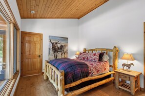 A wooden-framed bed with a plaid blanket, a wooden headboard, and a nightstand with a lamp and a horse figurine.