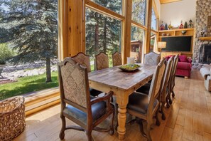A wooden dining table with chairs, a fireplace, and a view of trees.