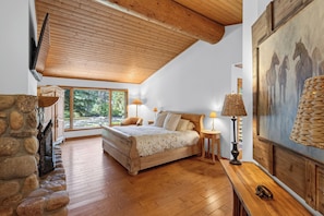 Quarto com uma cama grande, lareira de pedra, um quadro e vista para o exterior.
