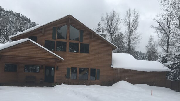 Een houten chalet met twee verdiepingen, een sneeuwbedekte dak en een groot raam op de bovenverdieping.