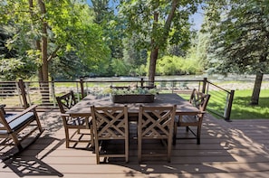 An outdoor deck with a table and chairs, surrounded by a railing, overlooking a river.