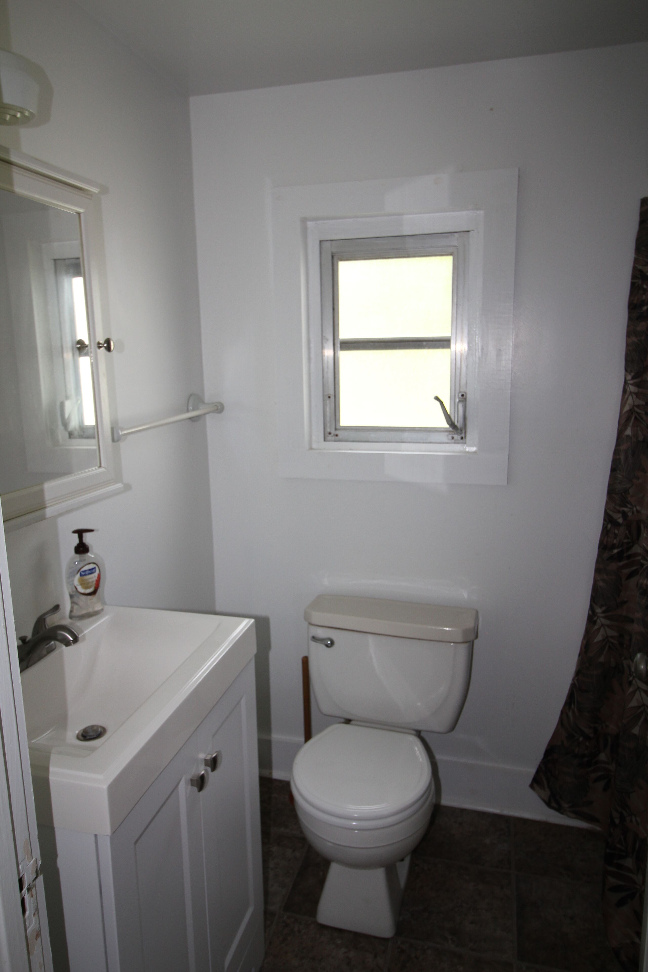A small bathroom with a toilet, a sink, and a window above the toilet.