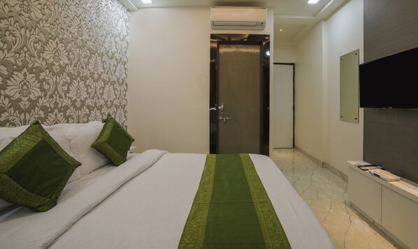 A hotel room with a bed, green pillows, a patterned wallpaper, a door, a flat-screen TV, and a marble floor.
