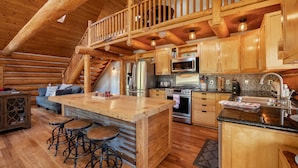 A rustic cabin interior with a wooden staircase, a central island with stools, and modern appliances.