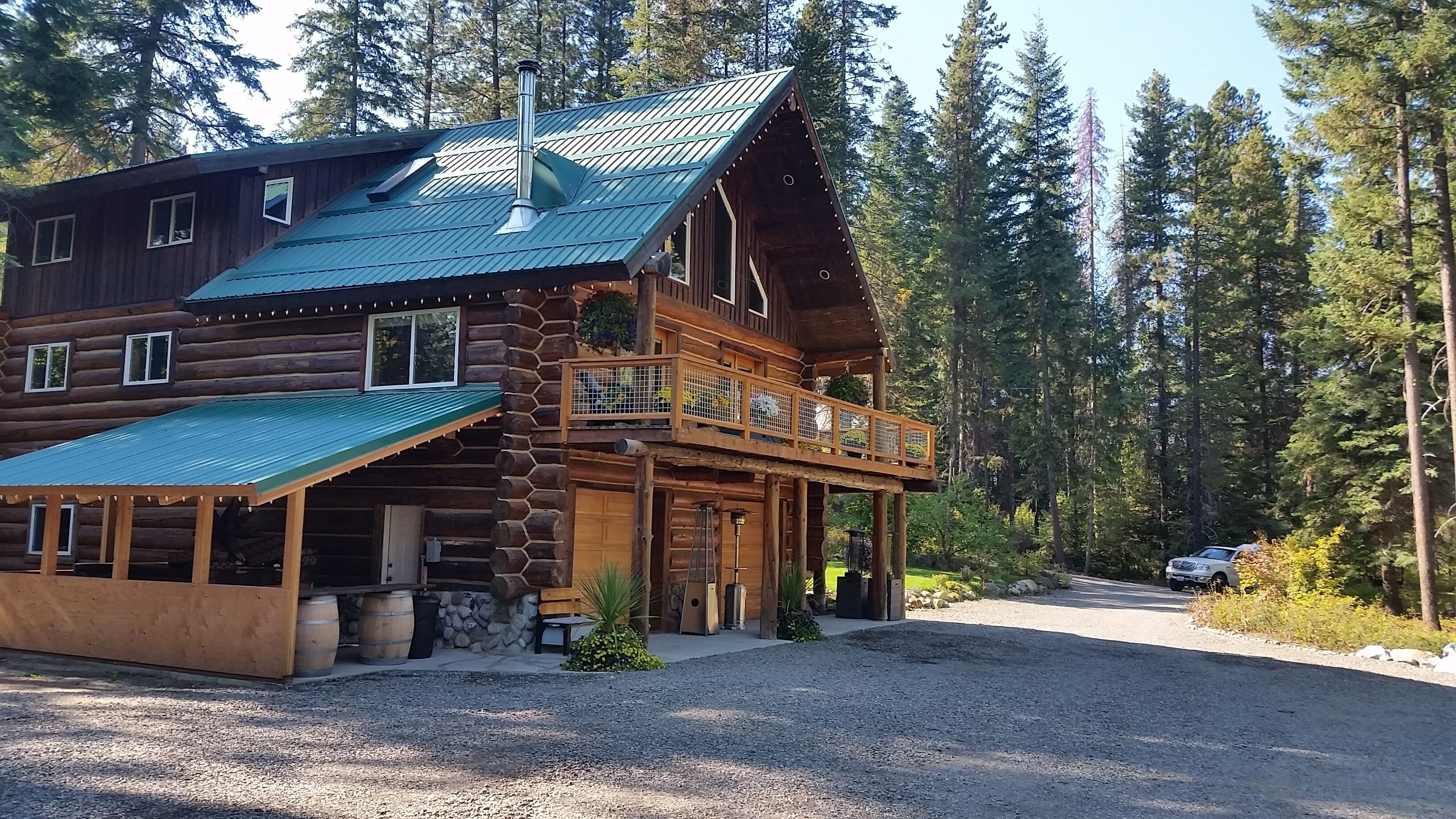 A log cabin with a metal roof, a balcony, and a gravel driveway.