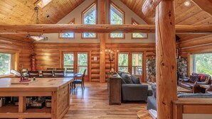 A spacious log cabin interior with a dining area, a sofa, and a stone fireplace.