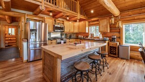 A spacious wooden cabin kitchen with a large island, stainless steel appliances, and a rustic wooden ceiling.