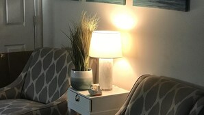 Habitació amb un sofà estampat, una petita taula auxiliar amb una làmpada, una planta en test i tres quadres a la paret.