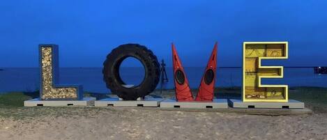 Une plage avec une grande sculpture en forme de pneu, un kayak et une structure en forme de lettre « E ».