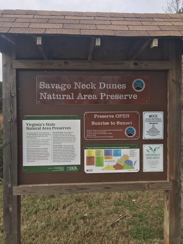 Un panneau d’information indiquant l’entrée de la réserve naturelle de Savage Neck Dunes, avec des renseignements sur les réserves naturelles de l’État de Virginie et les zones sous gestion environnementale.
