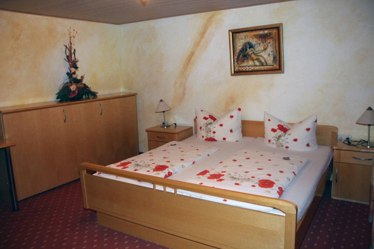 A bedroom with a wooden bed, a nightstand, a dresser, and a wall-mounted painting.