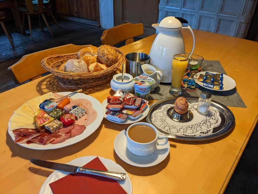 A breakfast setting with various food items, a coffee cup, and a jug of orange juice on a wooden table.