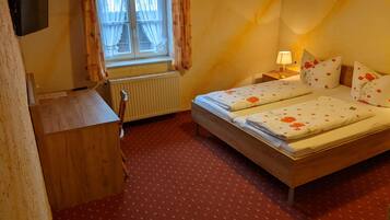 Een kleine, knusse kamer met een bed, een bureau, een radiator en een raam met gordijnen.