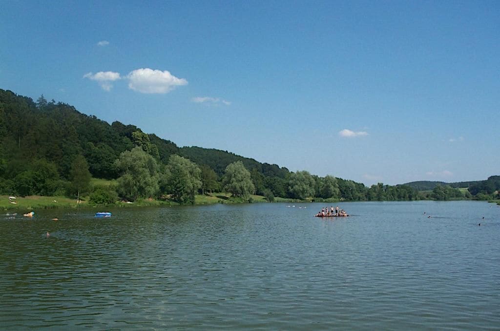 A calm lake with boats and a forested hillside in the background.
