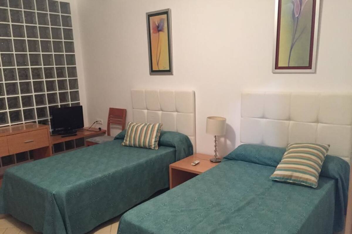 A room with two single beds, a TV, a small table, and a lamp.